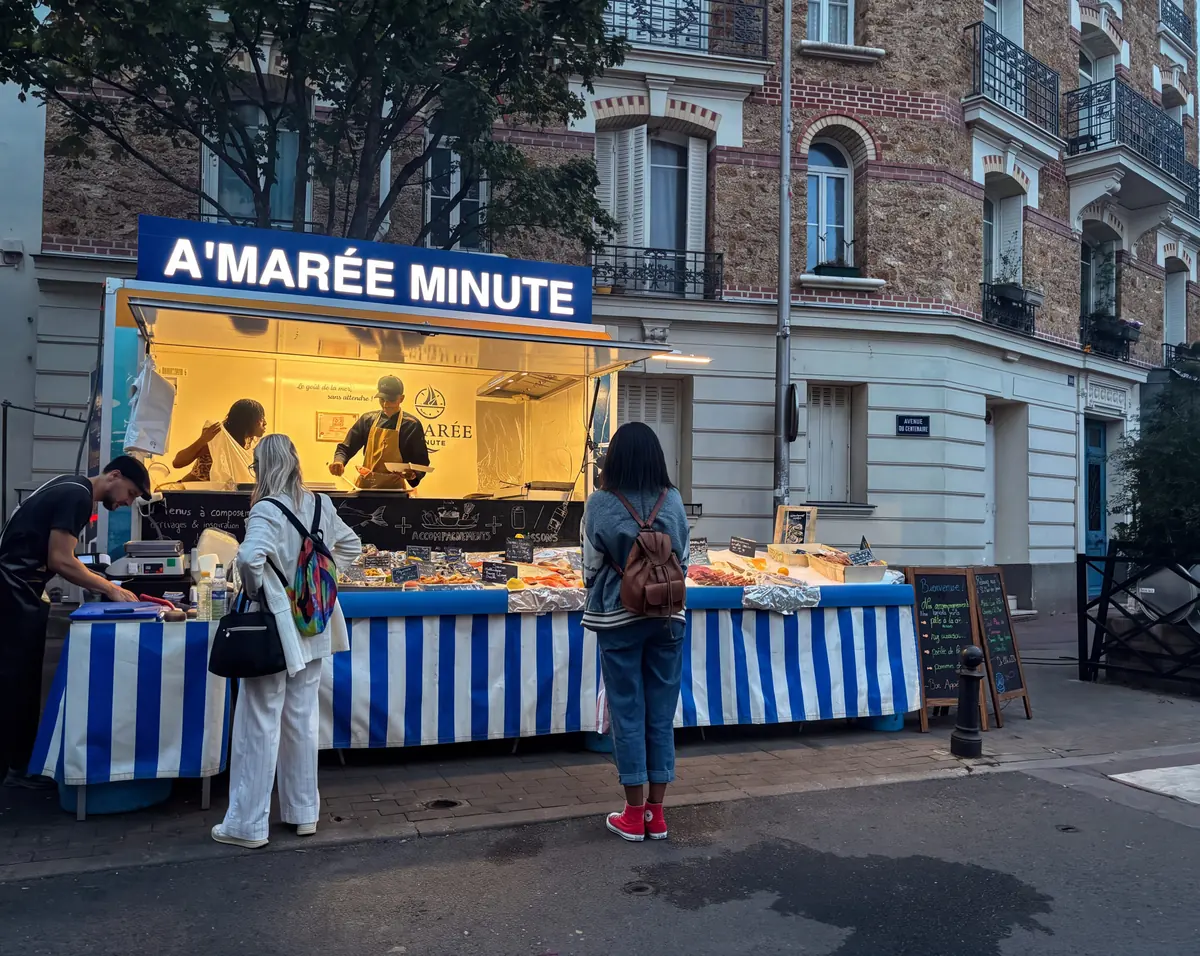 Le camion A'Marée Minute à la tombée du jour, son étal rayé bleu et blanc éclairé, l'équipe au travail et des clients devant.