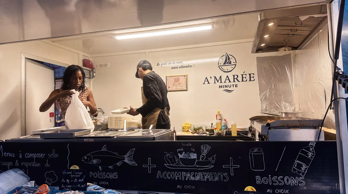 Dans le camion, l'équipe prépare les commandes derrière l'ardoise « Poissons au choix, accompagnements au choix, boissons ».