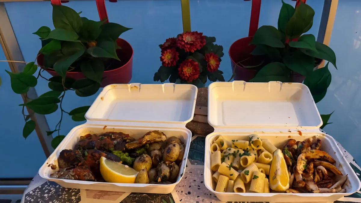 Deux barquettes ouvertes sur une table de balcon à l'heure bleue, des plantes et des fleurs rouges derrière.